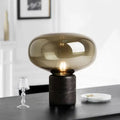 A sleek nordic table lamp with a translucent amber glass dome and a dark marble base for modern interiors