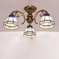 Antique brass three-arm semi flush mount ceiling fixture with blue and cream stained glass bell shades featuring geometric patterns