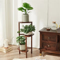 Dark wood bamboo corner plant stand with three circular shelves and slender legs holding green plants in ceramic pots