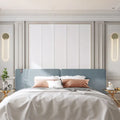 Contemporary gold oblong wall light fixture 110v 120v mounted above blue upholstered bed with white and rose gold pillows