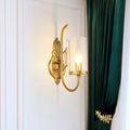 Contemporary gold wall light bedroom sconce with a gold-toned ornate design and clear glass shade with exposed bulb