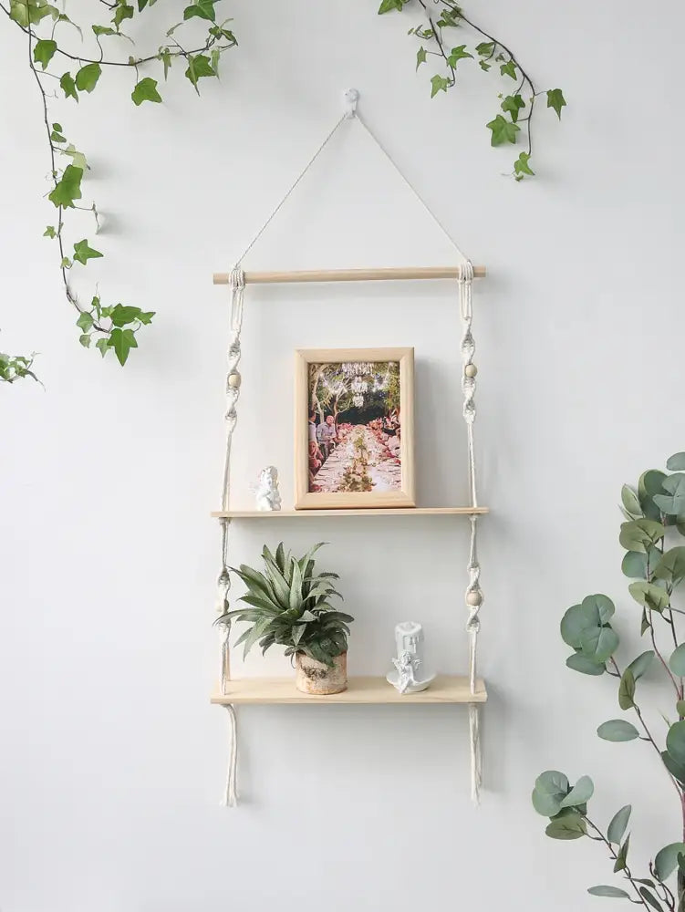 DecorBites™ boho macrame wall shelf with light wood shelves and white rope holding framed photo and potted plant for home decor