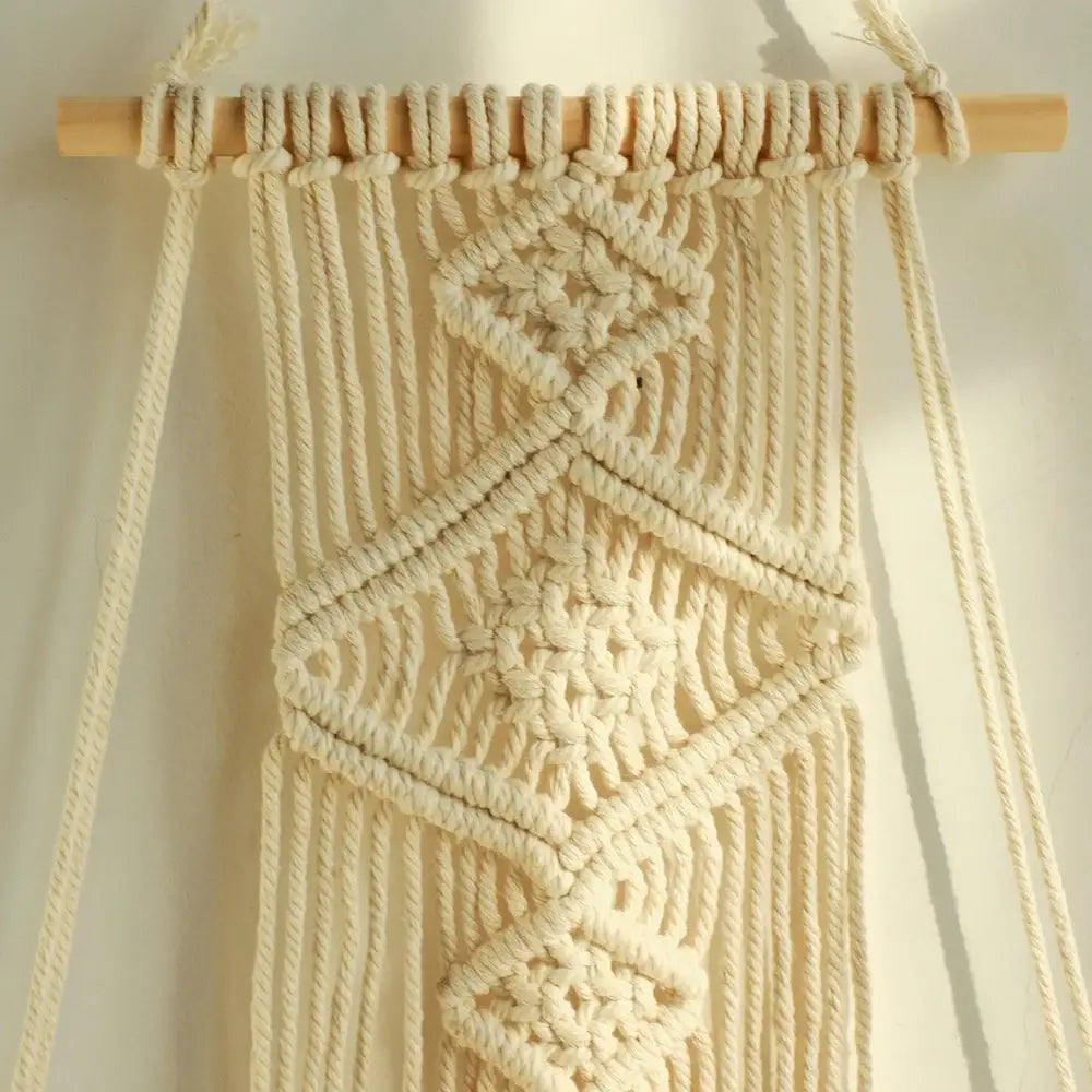 Cream-colored DecorBites™ boho macrame hanging shelf with geometric knotwork and natural wood dowel for home decor wall shelf