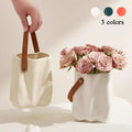 Cream-colored chic ceramic vase with textured wavy surface and brown leather handle for home decoration