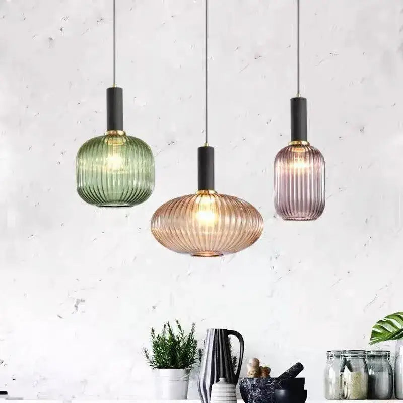 Three colorful glass pendant lights with amber green and gray ribbed shades hang above dining table by DecorBites