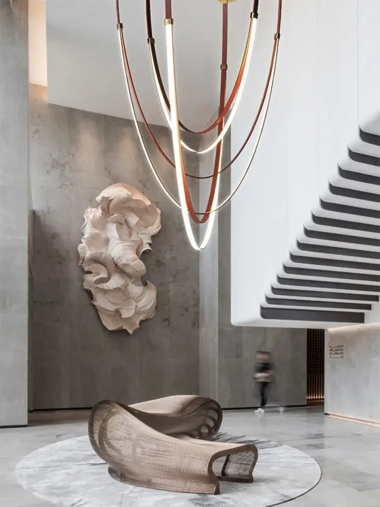 A sculptural beige lounge chair with woven mesh and curved metal frame on circular marble rug in decorbites flexible leather belt led chandelier light setting