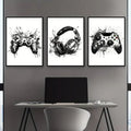 Three black-and-white graffiti gamepad canvas prints with splatter paint effects for gamer room decor above a desk