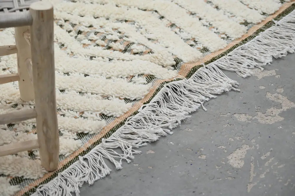 Cream-colored handmade moroccan azilal rug 240x155cm with textured geometric wool pattern and long white fringe edge