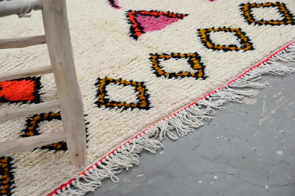 Cream-colored handmade moroccan azilal rug with bold pink orange black mustard geometric patterns and white tassel fringe