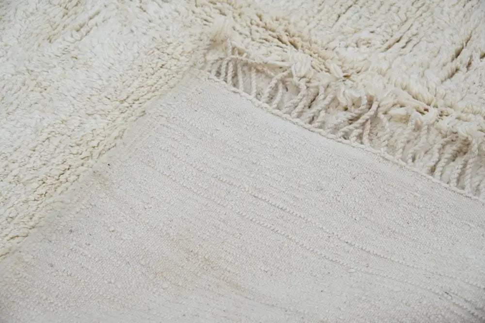 Cream-colored handmade moroccan azilal rug with textured wool surface and fringed edge 304 x 210 cm