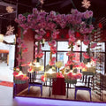 Pink artificial flower garlands hang from ceiling structure with decorbites™ industrial metal black island pendant light fixture height includes five bulb cage lanterns emitting warm light