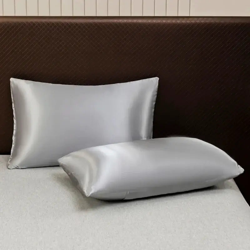 Two silver satin pillowcases from decorbites™ luxurious solid color bedding set on bed with dark brown headboard