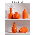 Set of five luxury modern ceramic orange vases with varied shapes and glossy finishes displayed on white shelves
