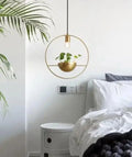 Gold-toned circular pendant light with a modern nordic planter featuring a hanging plant in a matching bowl