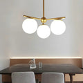 Gold-toned modern chandelier with three spherical white frosted glass shades for bedrooms by decorbites