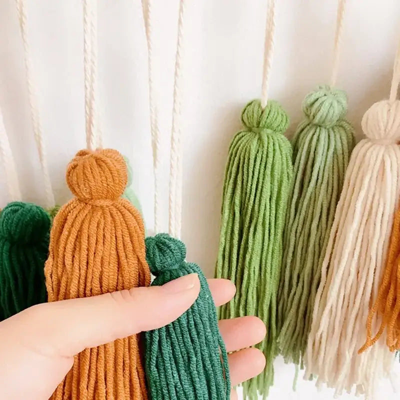 A hand holds colorful textured yarn tassels in earthy tones for a moroccan bohemian wall decor tapestry
