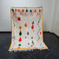 A vibrant cream-colored DecorBites™ moroccan handmade azilal rug with colorful geometric patterns and fringed edges