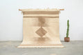 Beige and tan geometric-patterned moroccan handmade azilal rug with fringed edges hanging on wooden rod 300x200cm