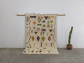 Beige moroccan handmade traditional azilal rug with black yellow green and orange geometric patterns on textured wool base