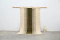 Beige and olive green moroccan handmade traditional azilal rug with woven texture and frayed edges hanging on wooden rod
