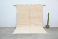 Beige moroccan handmade beni ouarain carpet with geometric pattern and fringed edges hanging on wooden rods