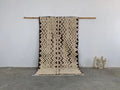 Beige and dark brown zigzag patterned moroccan handmade beni ouarain rug with fringed edges hanging on wooden rod