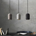 Three cylindrical cement pendant lamps in gray white and black with speckled finish hang against a textured wall industrial style