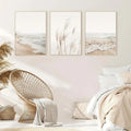Set of three beige-framed nordic seascape canvas wall art prints featuring soft coastal scenes and tall grasses