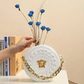 White circular handbag with gold chain strap and medusa head emblem in luxury fashion style nordic style flower vase half face