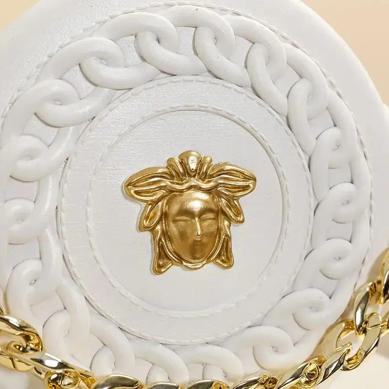 White leather handbag with gold tone medusa head clasp and braided chain strap complementing nordic style flower vase decor