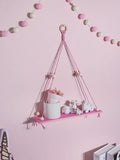 Pink green wooden macrame hanging shelf with wooden ring tassels holding white ceramic pot and miniature sheep for kids room