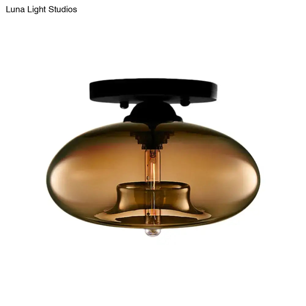 A sleek amber-tinted glass oval flush mount with black metal and exposed filament bulb for hallway lighting