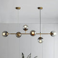 Modern brass finish pendant light with smoke grey glass and six spherical bulbs ideal for restaurants
