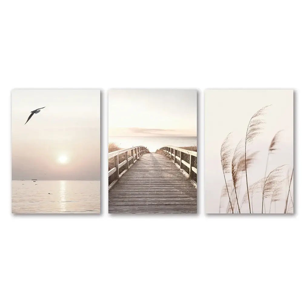 Set of three minimalist white seascape canvas prints featuring a seagull, boardwalk, and tall reeds by DecorBites™