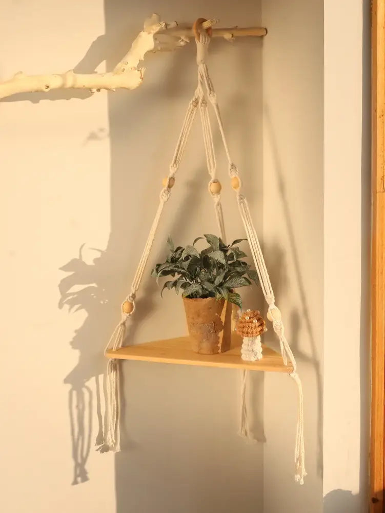 Beige macrame wooden corner shelf with wooden beads and tassels holding a potted plant boho wall decor