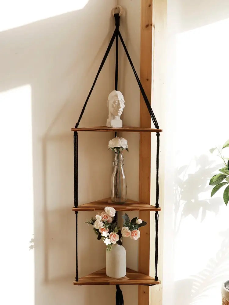 Black macrame cord suspends three wooden triangular shelves in a decorbites wooden corner shelf boho wall decor