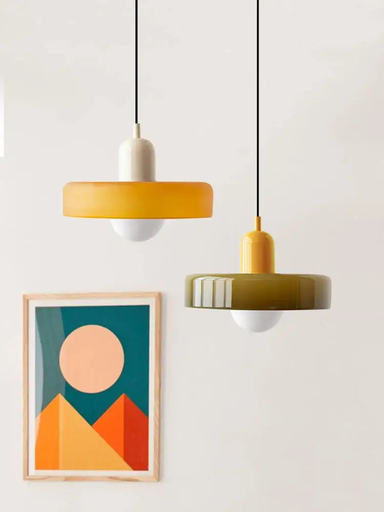 Two modern glass pendant lighting fixtures with matte yellow and olive green circular shades in Bauhaus style