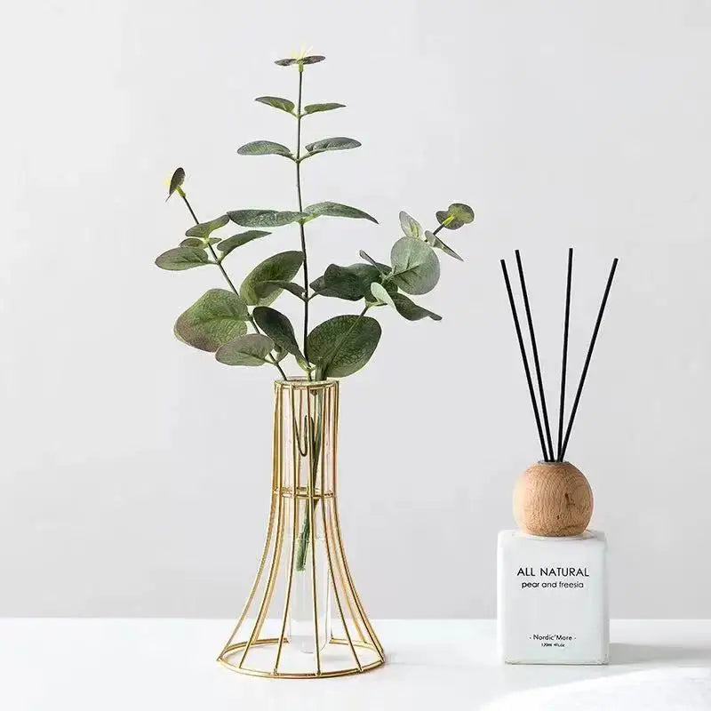 Gold wireframe vase holding green eucalyptus branches as modern desk decoration featuring metal flowers design