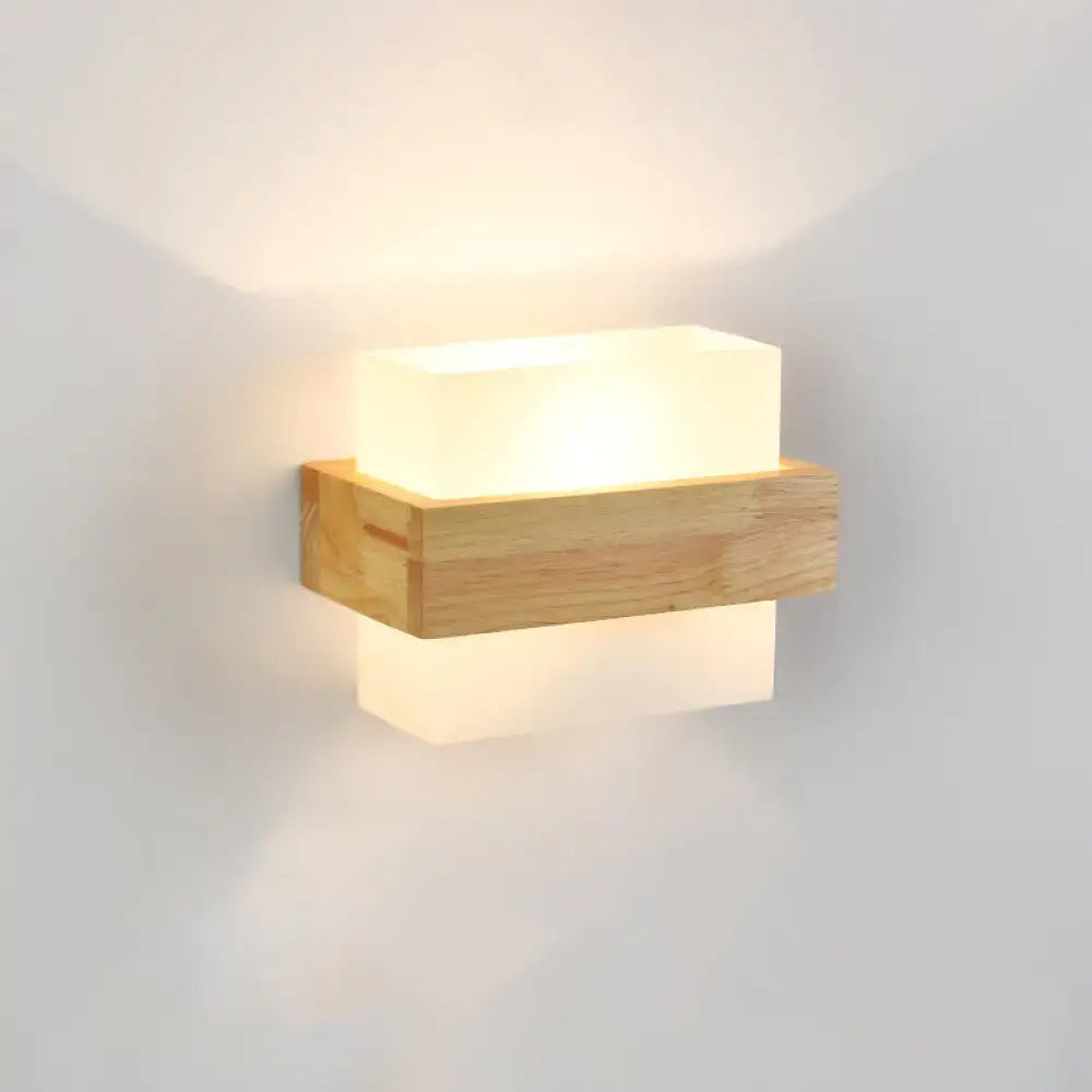 Minimalist brass and glass geometric wall sconce with warm translucent white diffuser on natural wood base for bedroom lighting