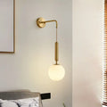 Minimalist gold finish wall light with a sleek curved arm and cream glass frosted globe shade for bedroom use