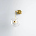 Minimalist gold-toned wall hanging light with clear glass globe and brass hardware for bedroom sconce lighting