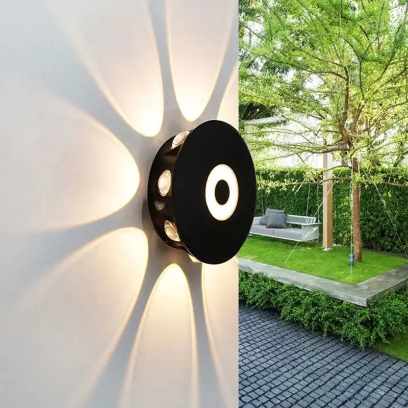 Modern black circular led outdoor wall sconce casting a warm radial glow on an outdoor wall for garden lighting