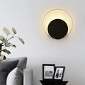 Modern black and gold metallic orbit sconce light with sleek center and warm rim emitting soft ambient light