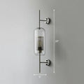 Modern black mesh wall mount lamp with clear glass cylinder and perforated metal interior on sleek black rods