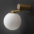 A sleek modern brass wall sconce with a frosted white glass sphere for bedroom lighting