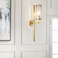 Modern brass cylinder sconce with clear water glass textured cylinder and sleek gold-toned metal arm bedroom lamp