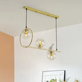 Modern brass global island lamp with three clear glass globes and a decorative white bird for dining room lighting