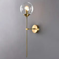 Modern brass pencil arm wall light with gold-toned finish, clear glass globe, and exposed bulb for bedroom use