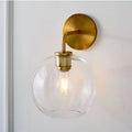 Modern brass wall lamp with sleek brass finish and clear white glass globe shade for bedroom lighting