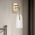 A sleek brass wall mount lamp with a clear glass bell-shaped shade and exposed filament bulb for bedroom use